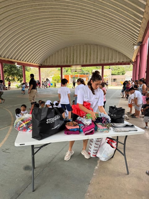 Woman organizing donated clothing at a table under a covered pavilion with children and people in the background at what appears to be a community donation event
