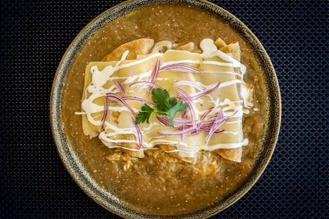 Bowl of brown curry soup topped with white noodles, sliced red onions, and cilantro on dark textured background