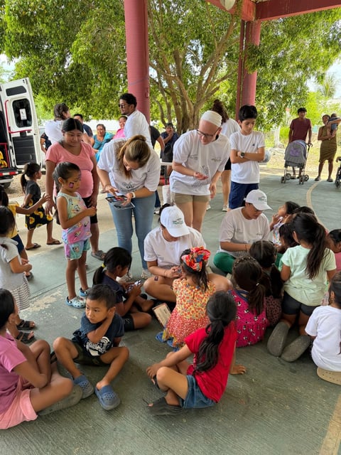 Adults and children gathered under a red pavilion for a community activity or event outdoors