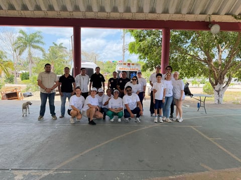 Group of students and adults posing together under a covered outdoor structure with tropical palm trees in background