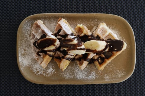 Plate of waffles with powdered sugar, chocolate drizzle, and sliced banana on a dark background