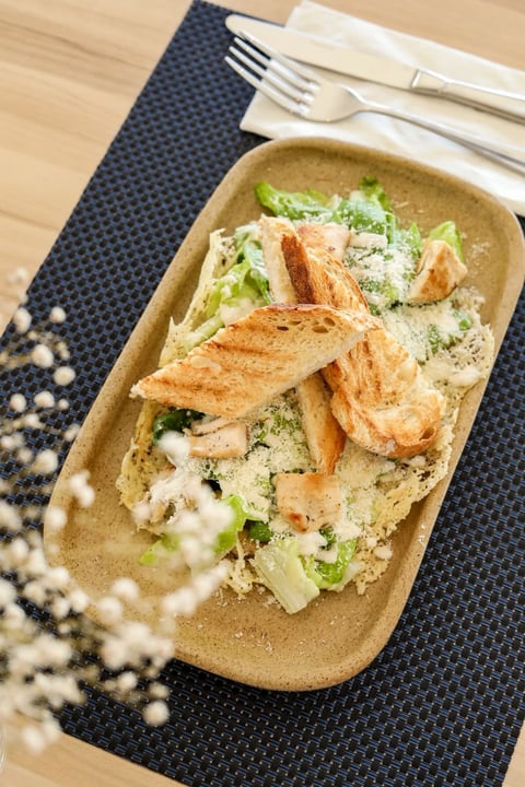 Caesar salad with grilled chicken breast and parmesan cheese in a tan bowl on a dark napkin with cutlery